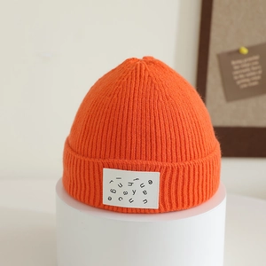 Detail of bright orange ribbed knit hat featuring a white letter patch and folded brim