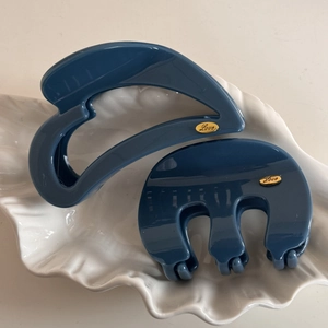 Detail view of blue resin hair claws with golden Love logo on a white ceramic tray