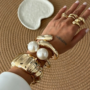 Close-up of chunky gold wrinkled alloy bracelets and large pearl open bangle set