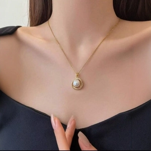 Elegante ciondolo rotondo dorato con perla bianca e cristalli scintillanti su modella