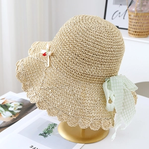 Detail of hand-woven beige straw hat with cherry bow and green plaid lace ribbon