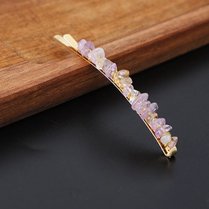 Detail of natural purple crystal stone hairpin on golden metal base over wood surface
