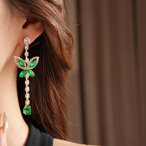 Close-up of golden drop earrings with green stones and zircons worn by a model
