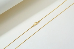 Close-up of golden stainless steel snake chain with lobster clasp on white background