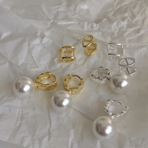 Detailed close-up of geometric hollow silver earrings and white pearls on white paper