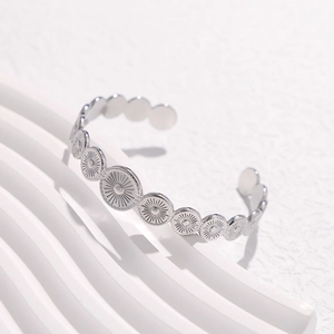 Detail shot of silver geometric open cuff with sunburst embossed patterns on white surface