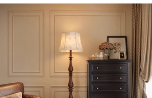 Close-up of a vintage floor lamp with a beige floral shade and a dark wood pole in a cozy room
