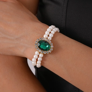 Close-up of double-row pearl bracelet with a large oval green gemstone and crystal halo