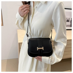Detail of black leather crossbody bag featuring a golden H-shaped metallic buckle and strap