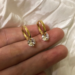 Detail of gold hoop earrings with sparkling zircon stones held on a fingertip