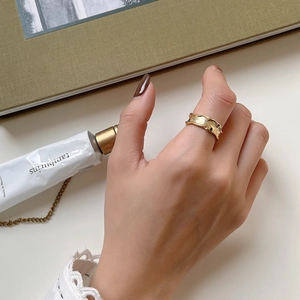 Close-up of golden irregular wavy ring with black gemstone accents worn on finger