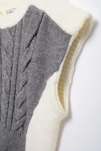 Detailed close-up of grey cable knit texture and cream ribbed neckline on this vest
