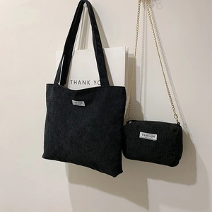 Detail of black corduroy tote bag set with small gold chain pouch and fashion label