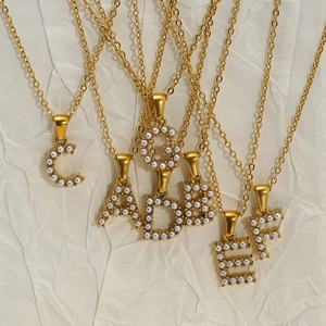 Golden 18K stainless steel initial necklaces with pearl inlay on white textured paper