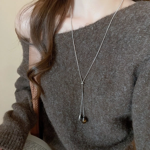 Detail of tiger eye and metal teardrop pendants on a long necklace against knitwear