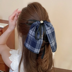Detail view of a blue and gray plaid bow hair clip with a small golden charm on brown hair