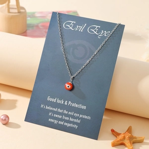 Detailed view of silver evil eye necklace with red bead pendant on a blue gift display card