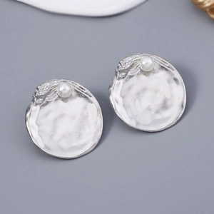 Detailed close-up of a silver hammered metal disc earring with a white pearl accent