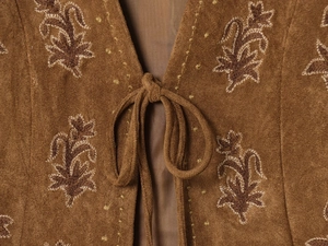 Détail du gilet en daim marron avec broderie florale délicate et fermeture à lacets