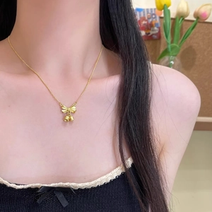 Detail of elegant gold bow and bell pendant necklace on woman's collarbone