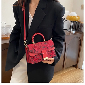 Détail du sac rouge en dentelle avec broderie papillon porté par un mannequin en blazer noir