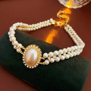 Detail of double-layer white pearl bracelet with gold rhinestone oval centerpiece