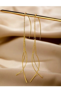 Detail of elegant gold tassel earrings hanging over soft white satin fabric background