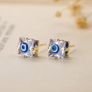 Macro detail of gold-plated evil eye stud earring with clear crystal and blue enamel