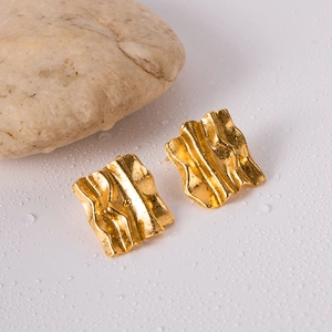 Macro shot of gold square stud earrings with ripple texture on a wet stone surface