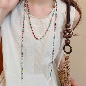 Detail of colorful beaded necklace with white pearls paired with a woven handbag