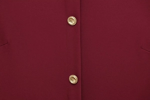 Detail view of burgundy crepe fabric texture with decorative gold hammered buttons
