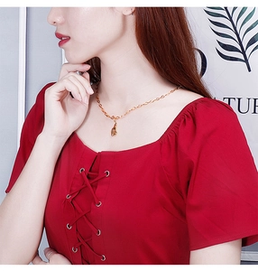 Gros plan d'un collier cœur en titane doré porté par un mannequin en haut rouge