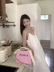 Detail of pink woven straw tote bag with Paris lettering shown with white dress