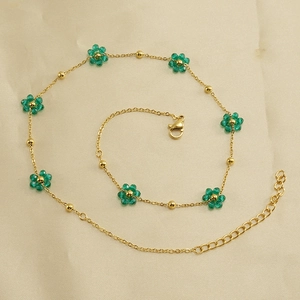 Detailed view of the gold chain bracelet featuring green beaded flower charms on fabric