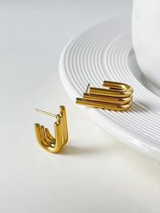 Macro shot of gold-plated triple-layer U-shaped hoop earrings on a white porcelain plate