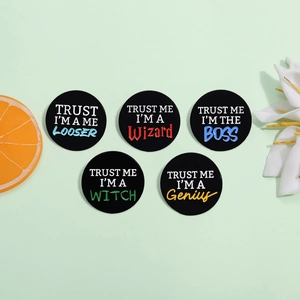 Set of five circular black metal pins with funny English slogans on a green surface