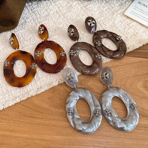 Three pairs of acrylic hoop earrings with silver cross accents on a knit texture