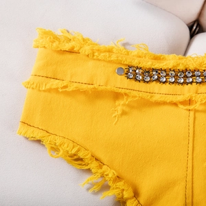 Dettaglio di pantaloncini di jeans gialli con bordi sfilacciati, rivetti e decori di paillettes