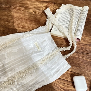 Gros plan sur la toile blanche texturée du sac avec franges florales et étiquette dorée