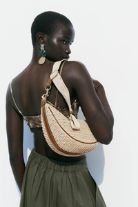Detail of woven crescent shoulder bag with brown leather trim and canvas strap on model