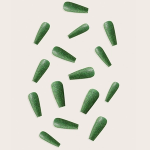 Macro shot of long green glitter press-on nails on a clean beige background