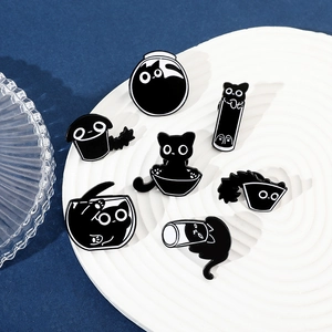 Set of eight cartoon black cat enamel pins displayed on a white ceramic tray