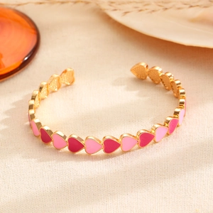 Detalle de una pulsera de corazón dorada con eslabones de esmalte rosa y rojo sobre tela