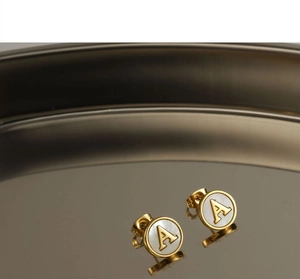 Detail shot of golden round stud earrings featuring a white shell inlay and letter A