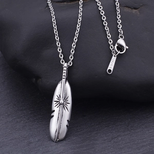 Minimalist stainless steel feather pendant necklace with sun engraving on a rock background