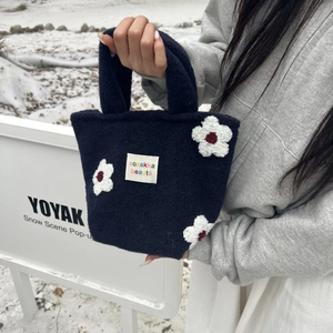 Detail of plush navy blue wool tote bag with white 3D floral embroidery in snowy setting