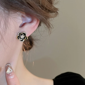 Gros plan de boucles d'oreilles camélia noir avec bords dorés et cristaux sur l'oreille