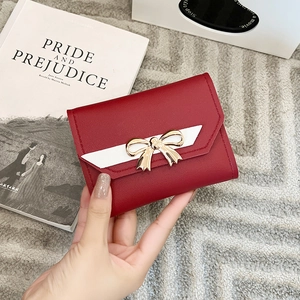 Close-up of red tri-fold wallet featuring a white and gold leather bow on a book background