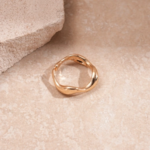 Detail of a wavy irregular gold ring on a marble surface with natural stone accent