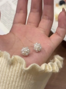 Detail of elegant pearl cluster stud earrings held by hand to show size and texture